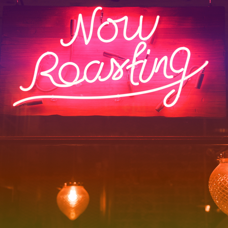 A neon sign of the words "Now Roasting" with decorative lights below